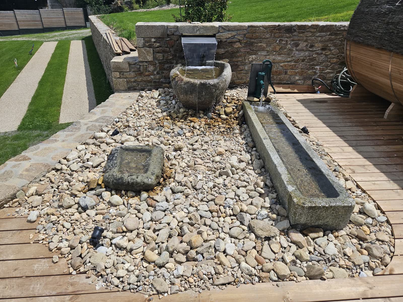 Lame d’eau inox dans un mur de pierre sèche, auges de ferme en granit et terrasse bois — Guipavas